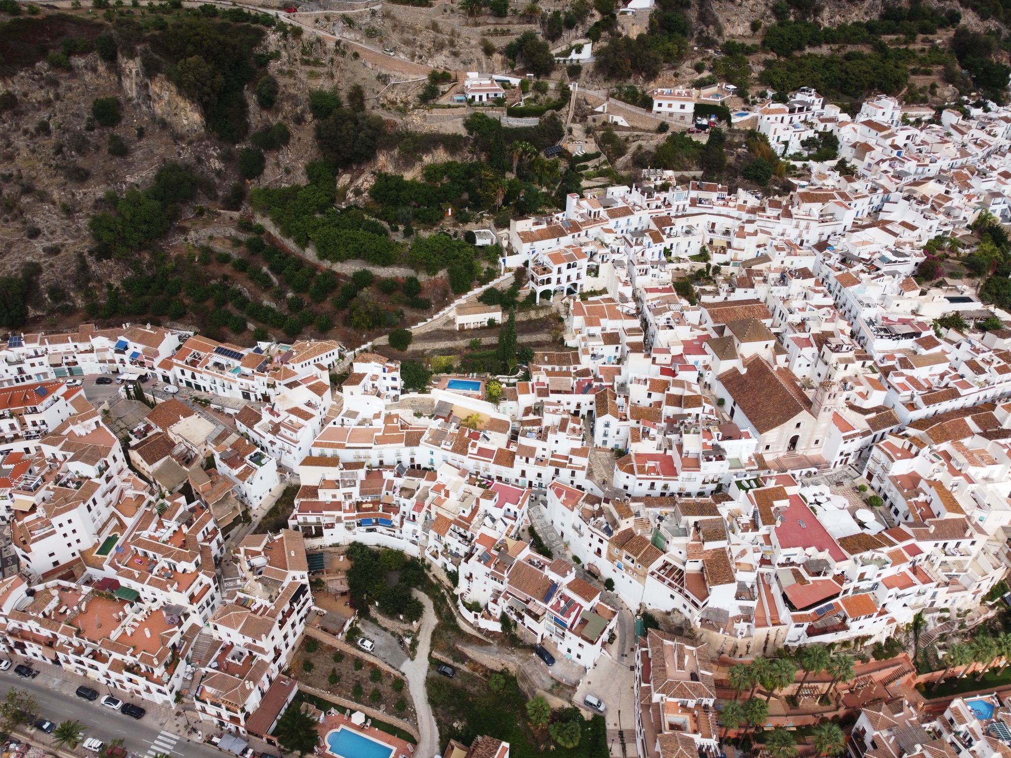 Vue aérienne de Frigiliana accrochée au flanc de la Sierra Almijara — le village et les pentes au-dessus, où se dressait El Fuerte en 1569