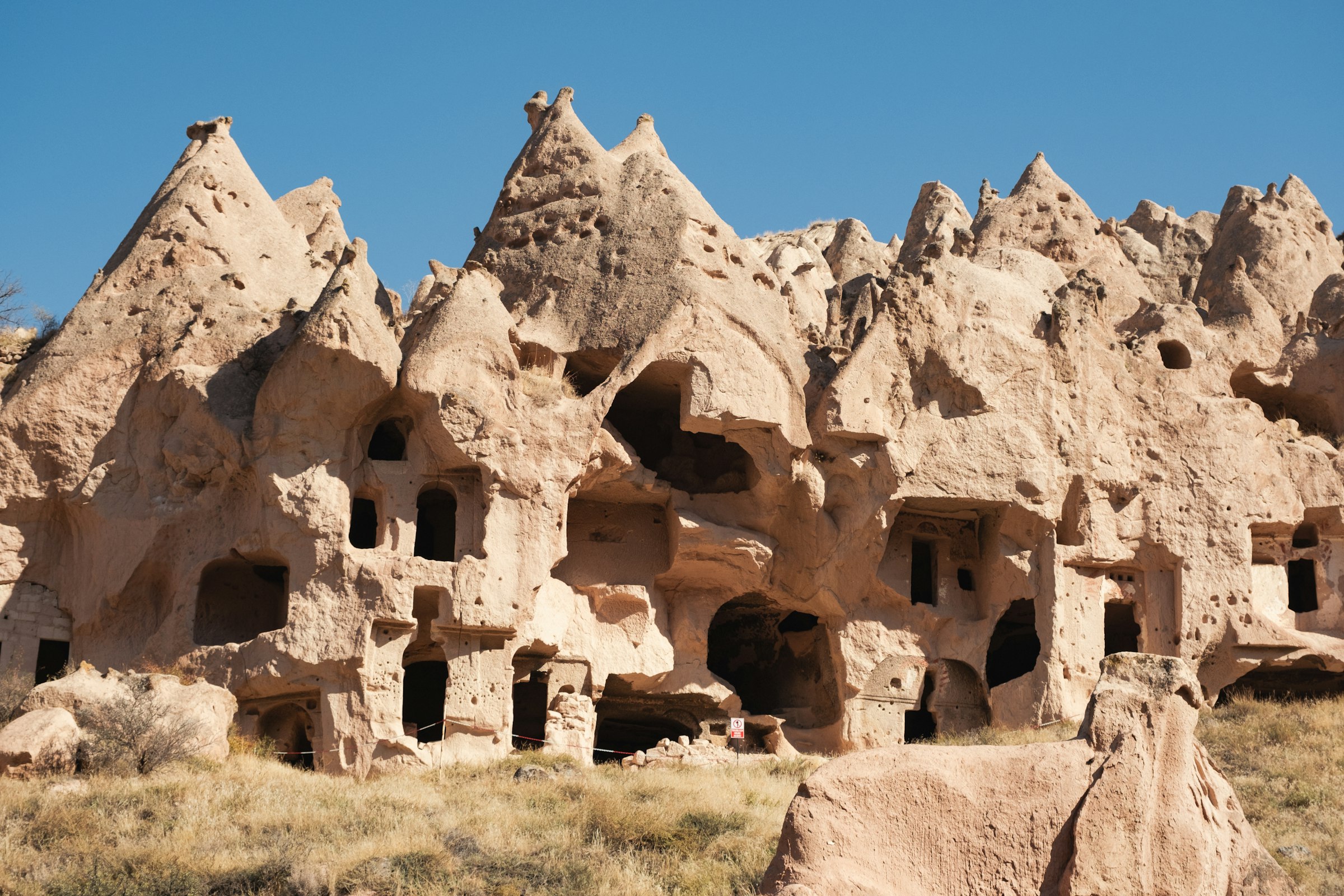 Des cheminées de fée de Cappadoce abritant des habitations troglodytes creusées dans la roche, sous un ciel clair.