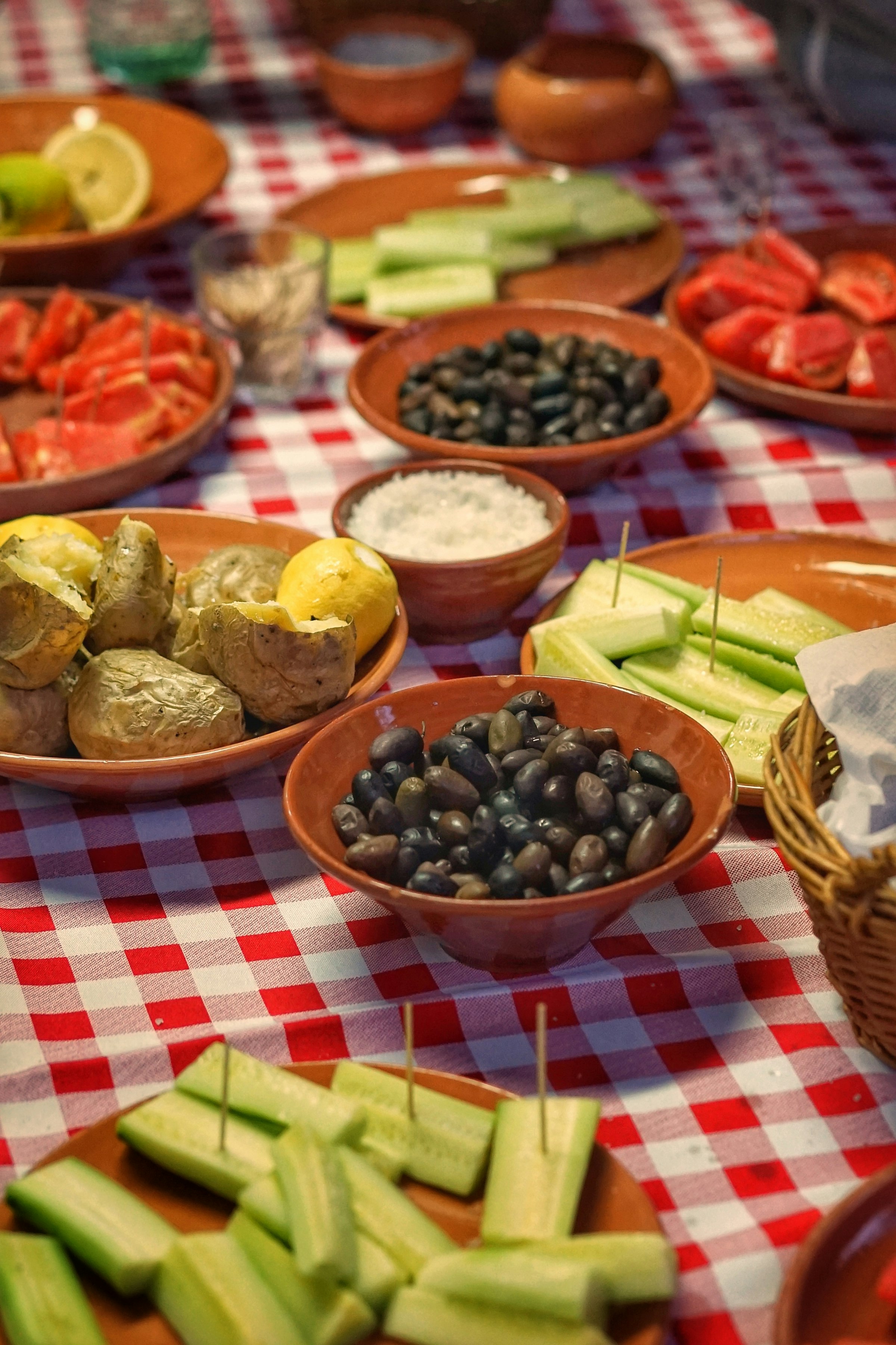 Un assortiment de mezedes crétois sur une nappe à carreaux rouges : pommes de terre au four, olives noires, une trempette, des bâtonnets de concombre et un demi-citron