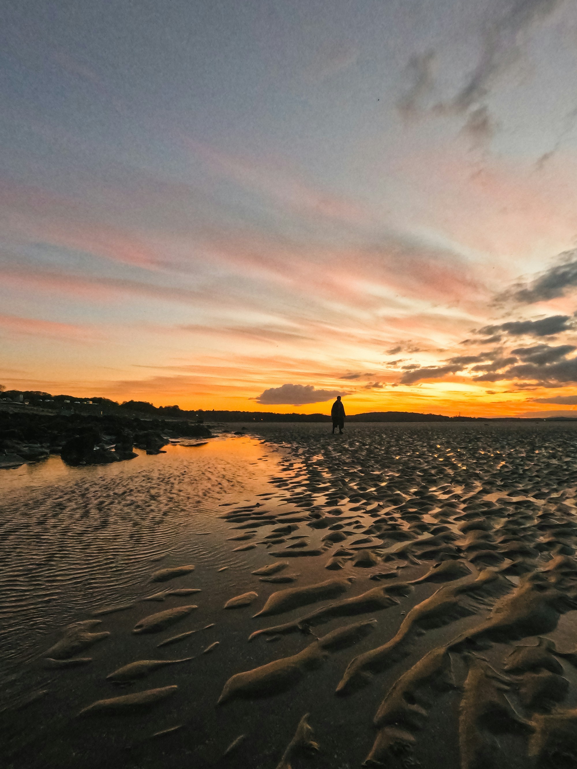 A person walking on a wide sandy beach at sunset