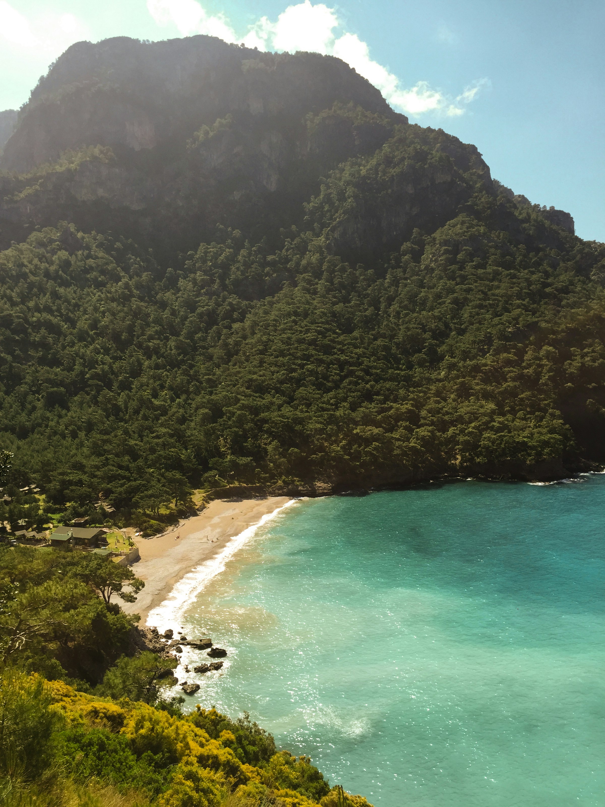 La crique de Kabak Bay : une plage au creux d'une montagne couverte de pins, une eau turquoise lumineuse, quelques camps à la lisière des arbres.