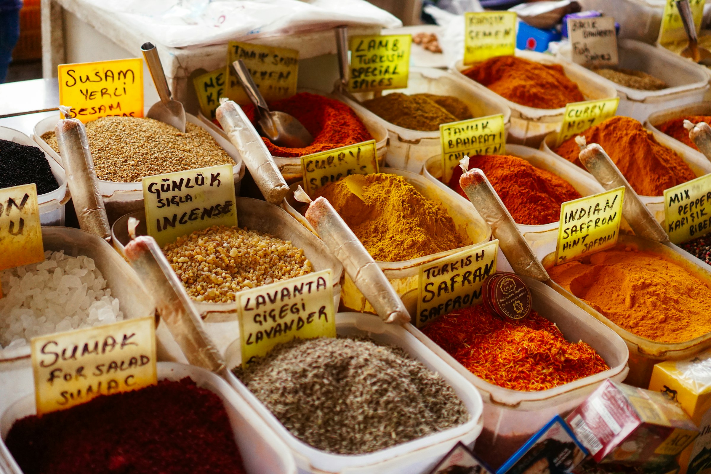 Un étal d'épices d'un marché turc : safran, sumac, lavande, curry en plateaux colorés avec leurs étiquettes en turc.