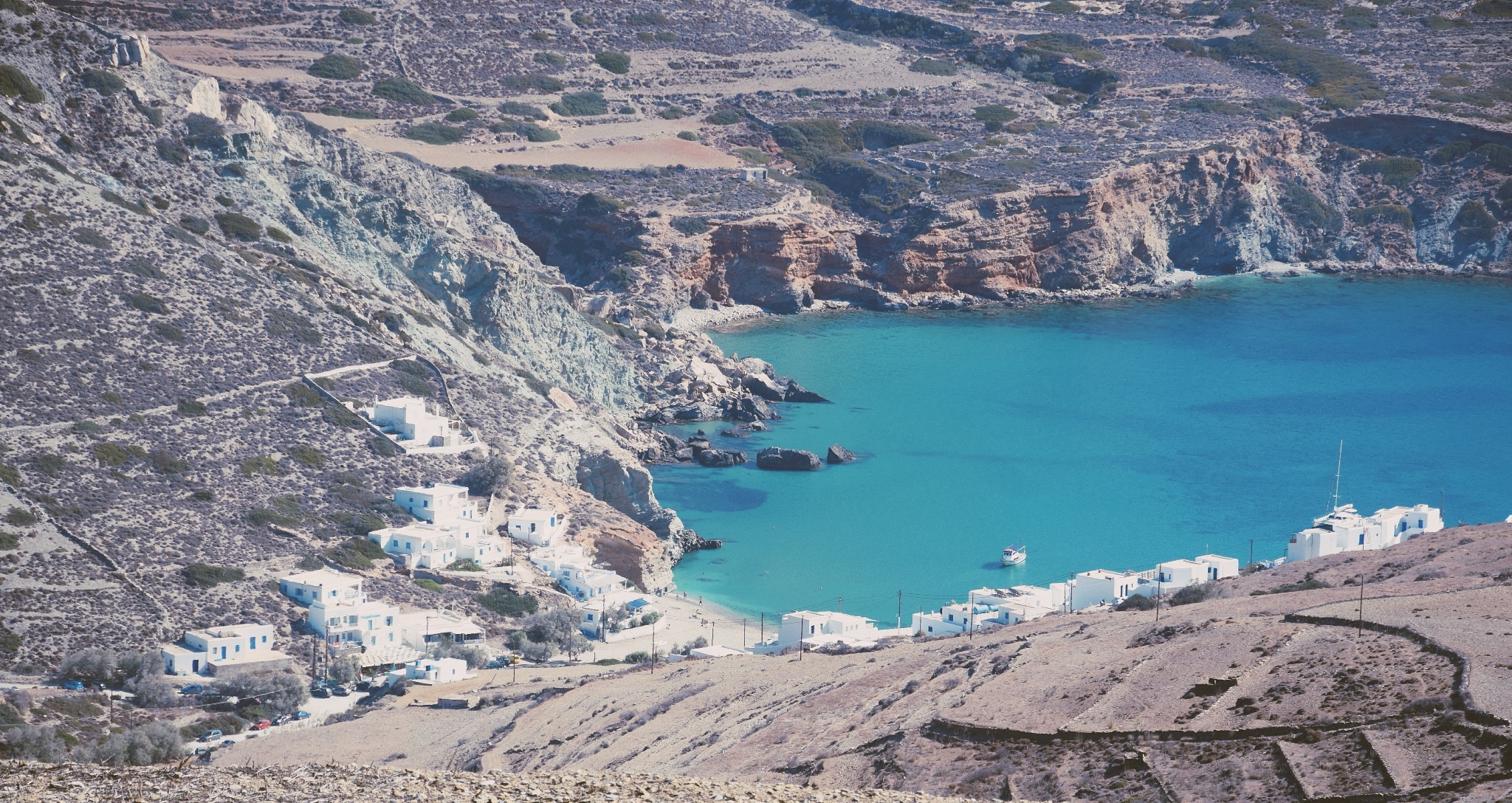 La baie d'Agali à Folegandros vue d'en haut : une anse d'eau turquoise, quelques maisons blanches éparpillées sur les pentes rocheuses et arides qui descendent vers la mer