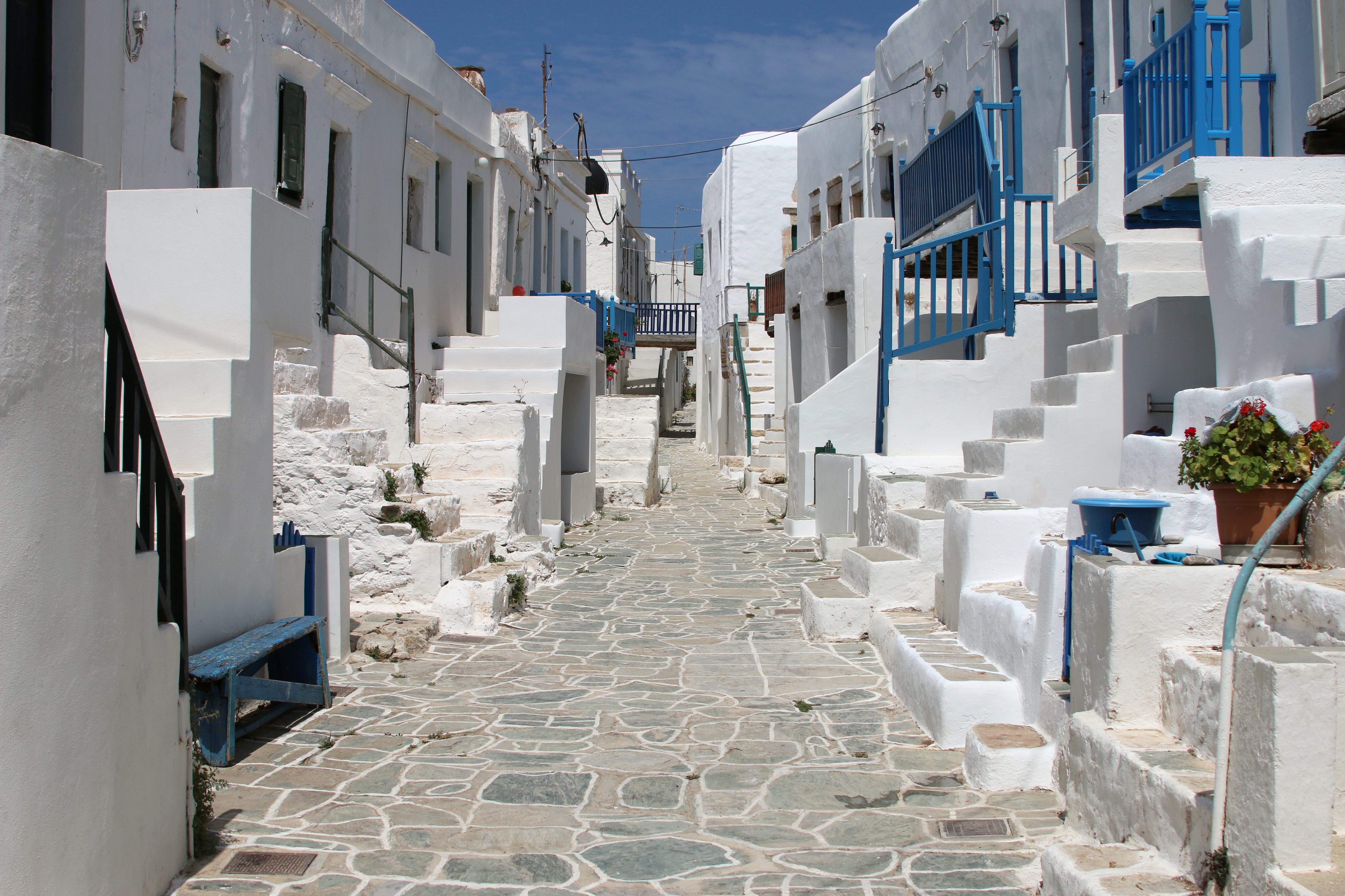 Une ruelle pavée du quartier médiéval du Kastro de Folegandros, maisons blanches aux balustrades bleues et géraniums rouges