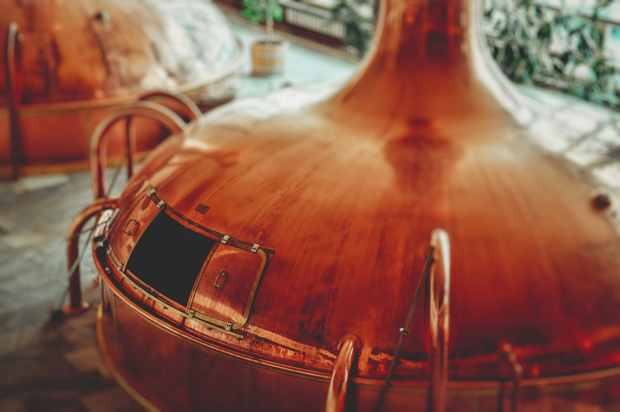 A close-up of a large copper pot still with its swan-neck rising, in a distillery still room.
