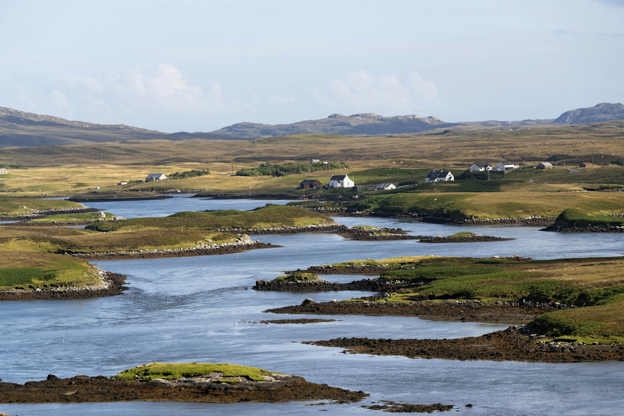 A view over interlocking sea lochs and lochans cutting through rocky moorland, white-walled croft houses scattered along the low hills.