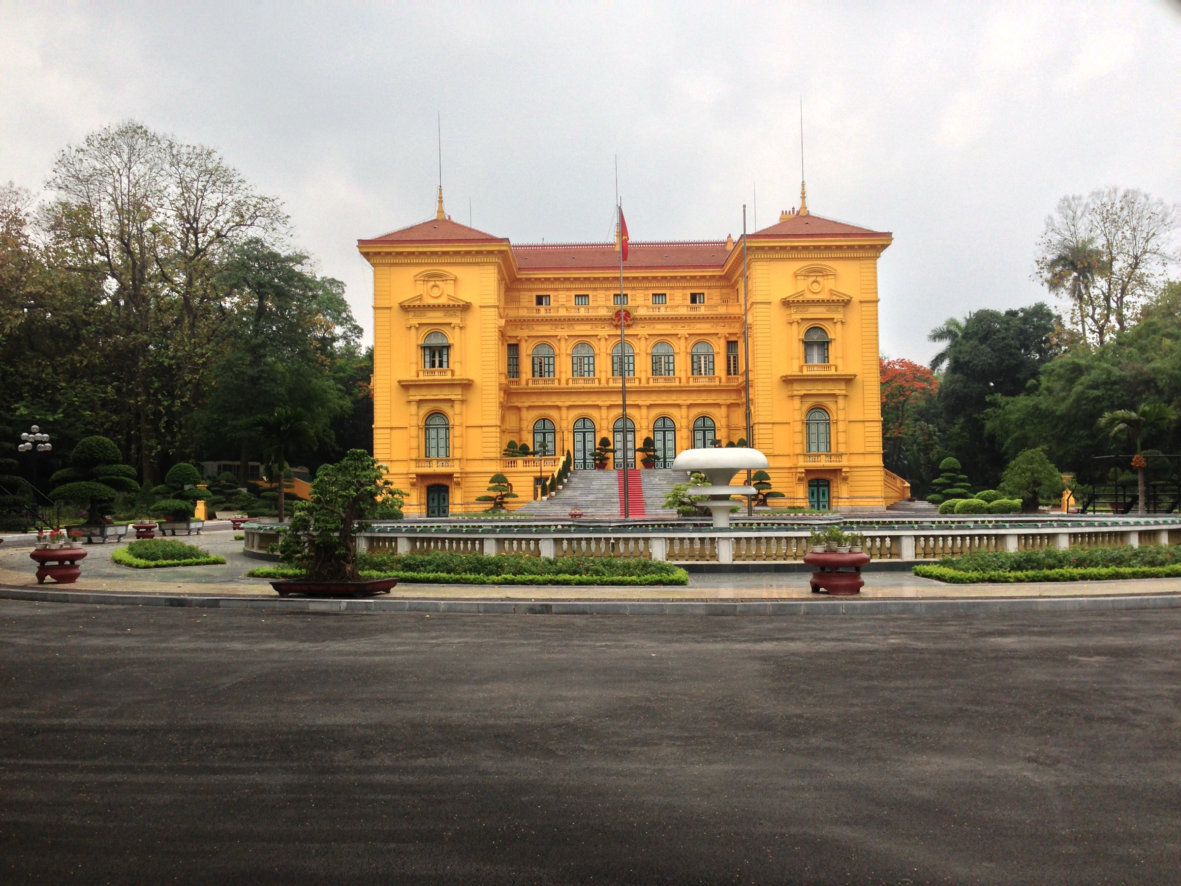 Palais présidentiel de Hanoi — bâtiment colonial français à la façade jaune ocre et toit rouge, jardins taillés, bonsaïs et topiaires devant