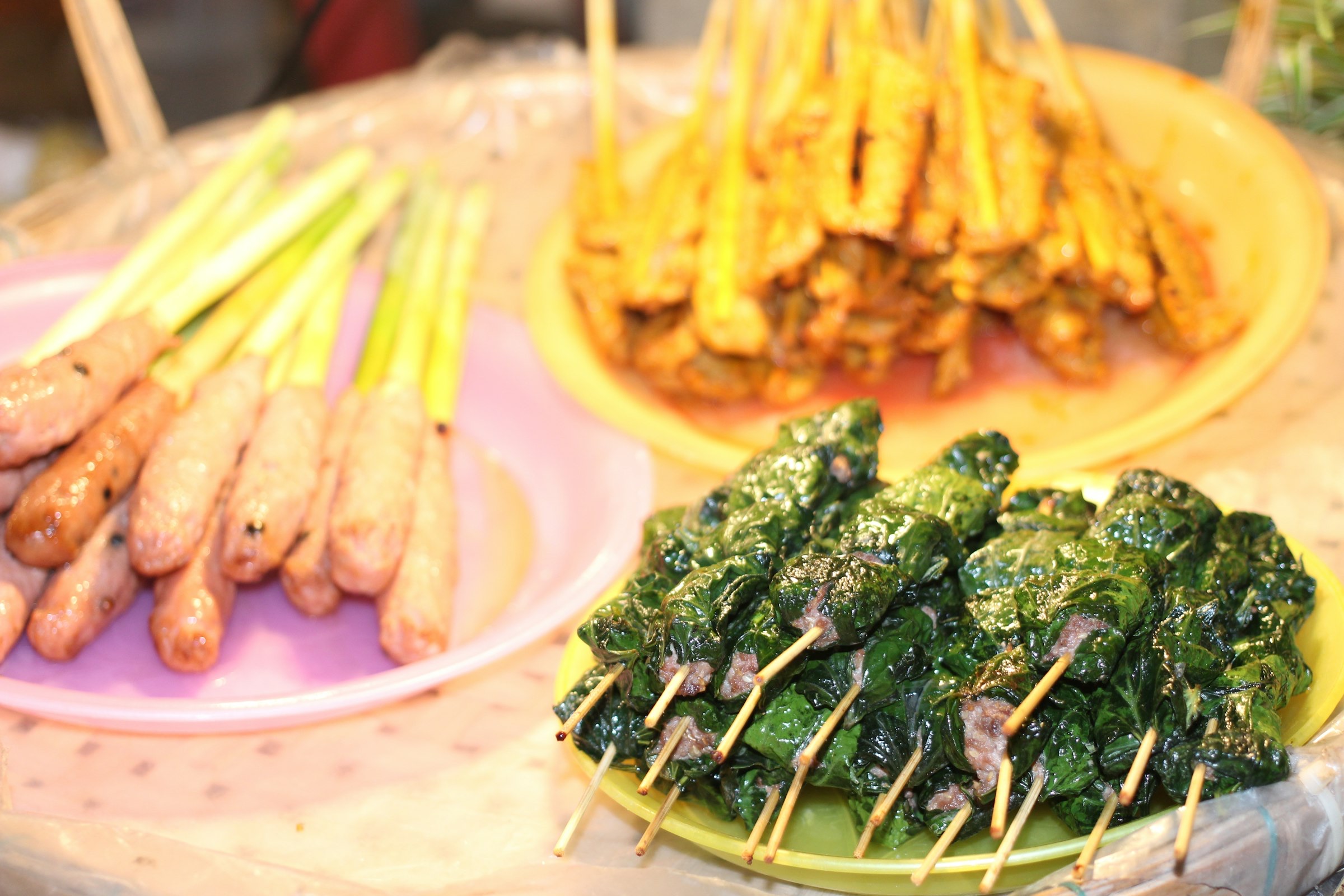Brochettes de rue au marché de nuit de Hội An — bœuf lolot, saucisses grillées et brochettes de poulet présentées sur assiettes colorées rose, jaune et vert