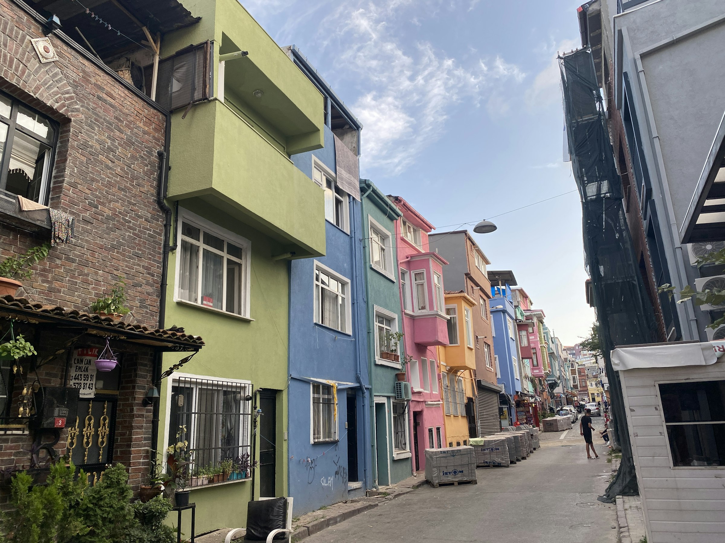 Une rue étroite de Balat bordée de maisons aux façades colorées — vert, bleu, rose, jaune — un passant au loin, en plein jour.