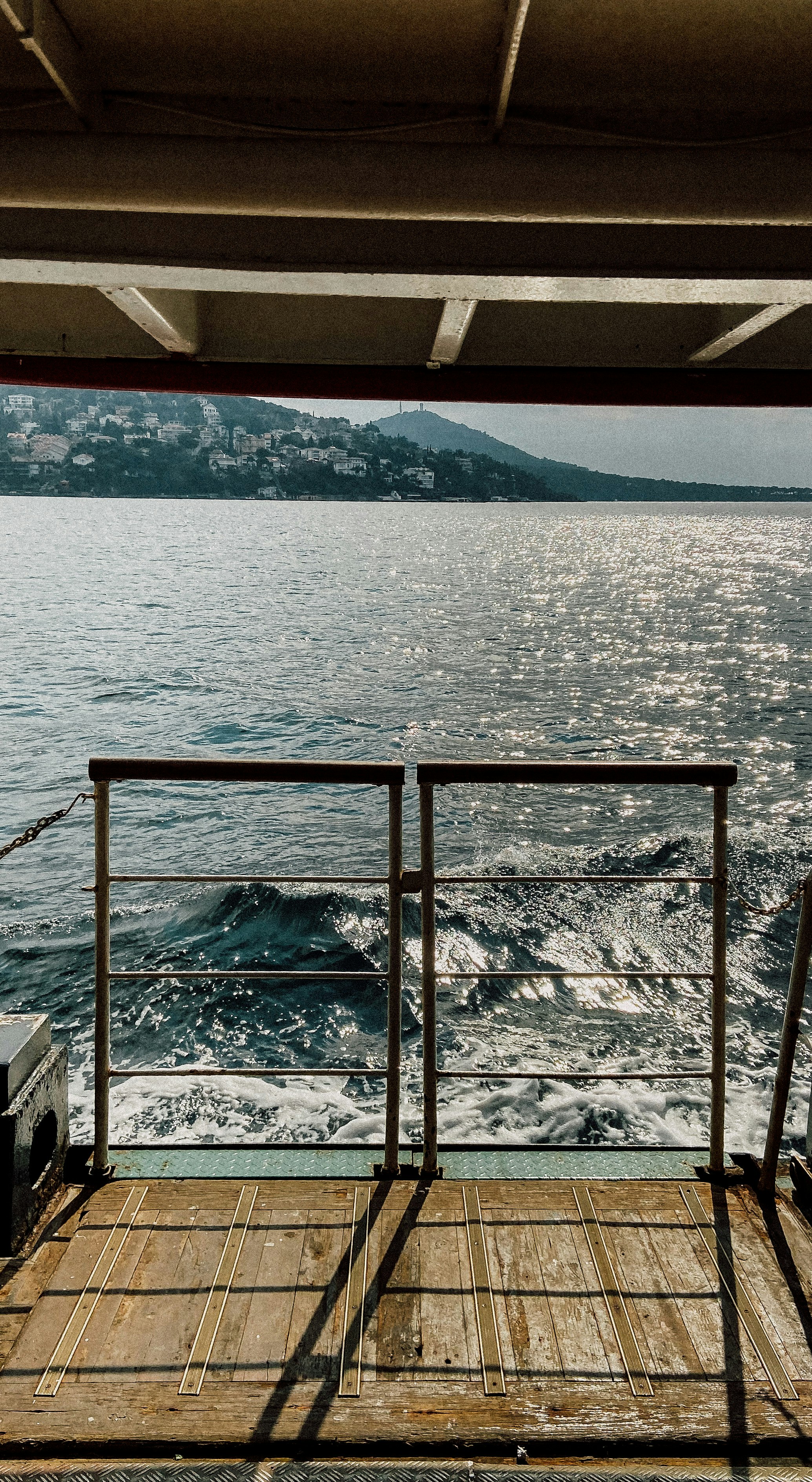 Le sillage d'un ferry sur le Bosphore, vu de l'arrière depuis le pont en bois, les collines habitées de la rive au loin.