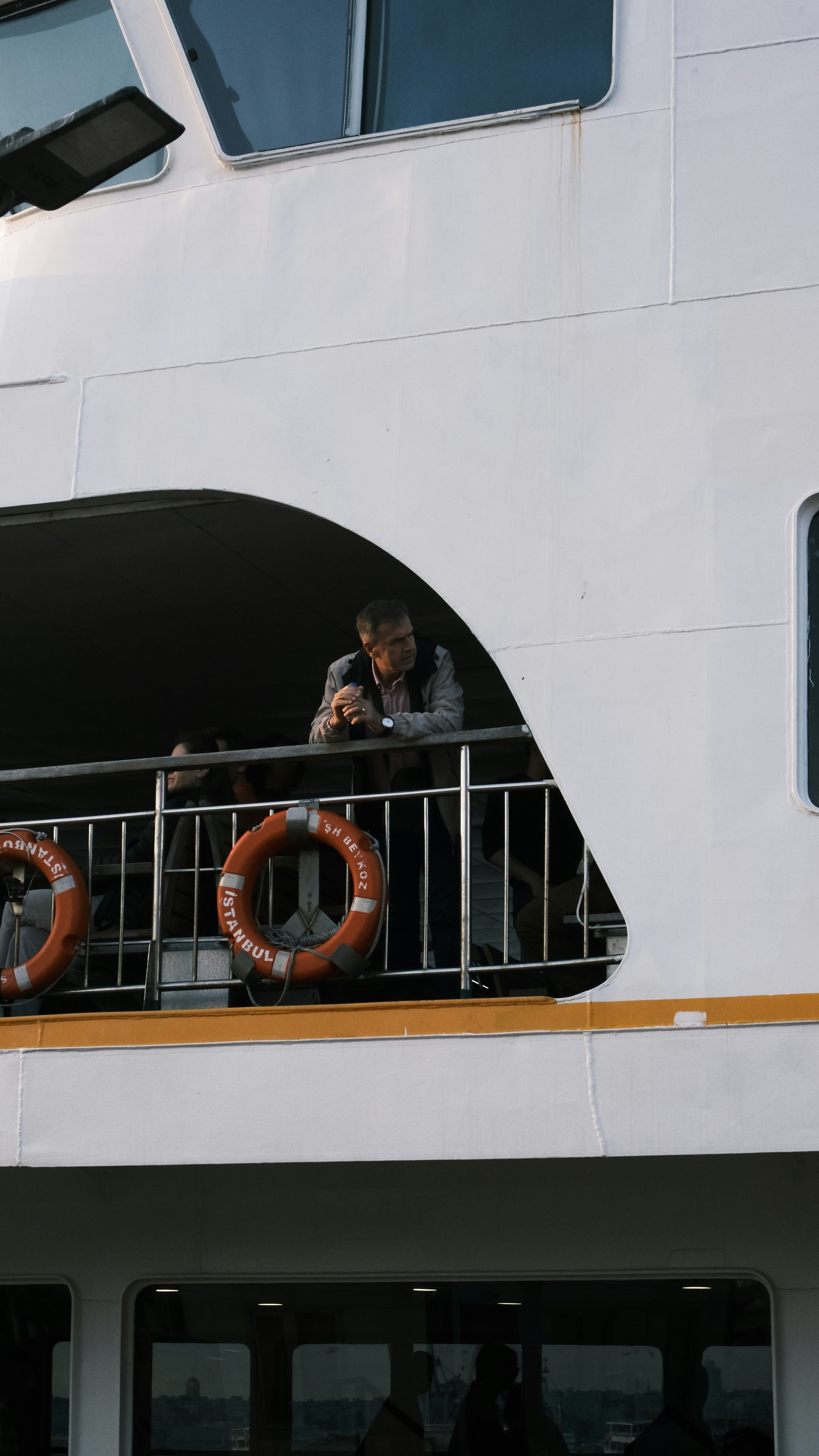 Un passager accoudé au bastingage d'un ferry public d'Istanbul, des bouées de sauvetage orange marquées « İSTANBUL » fixées à la rambarde.