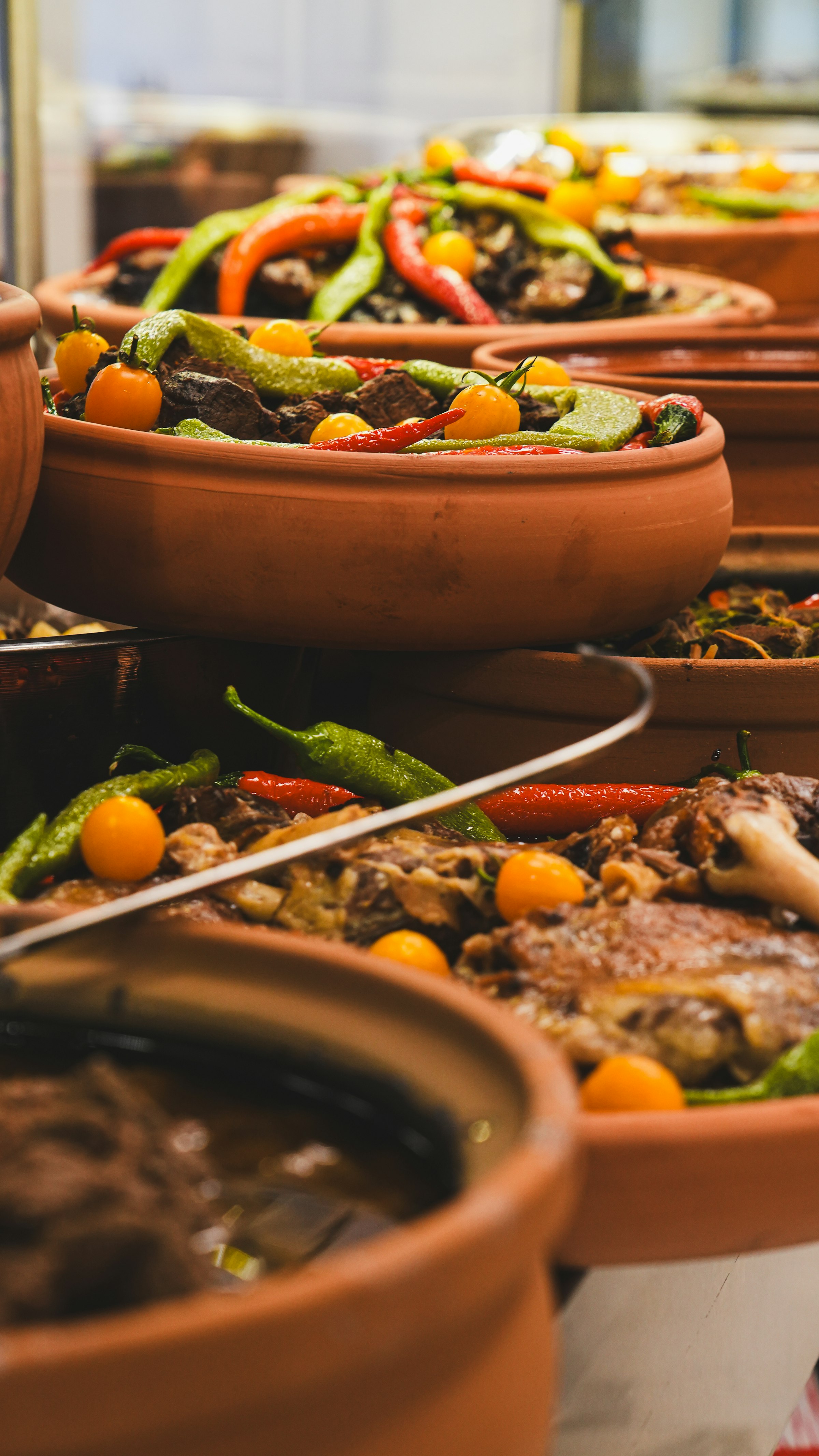 Des plats turcs mijotés en cocottes de terre cuite — agneau, poivrons verts et rouges, tomates cerises jaunes — alignés pour le service.