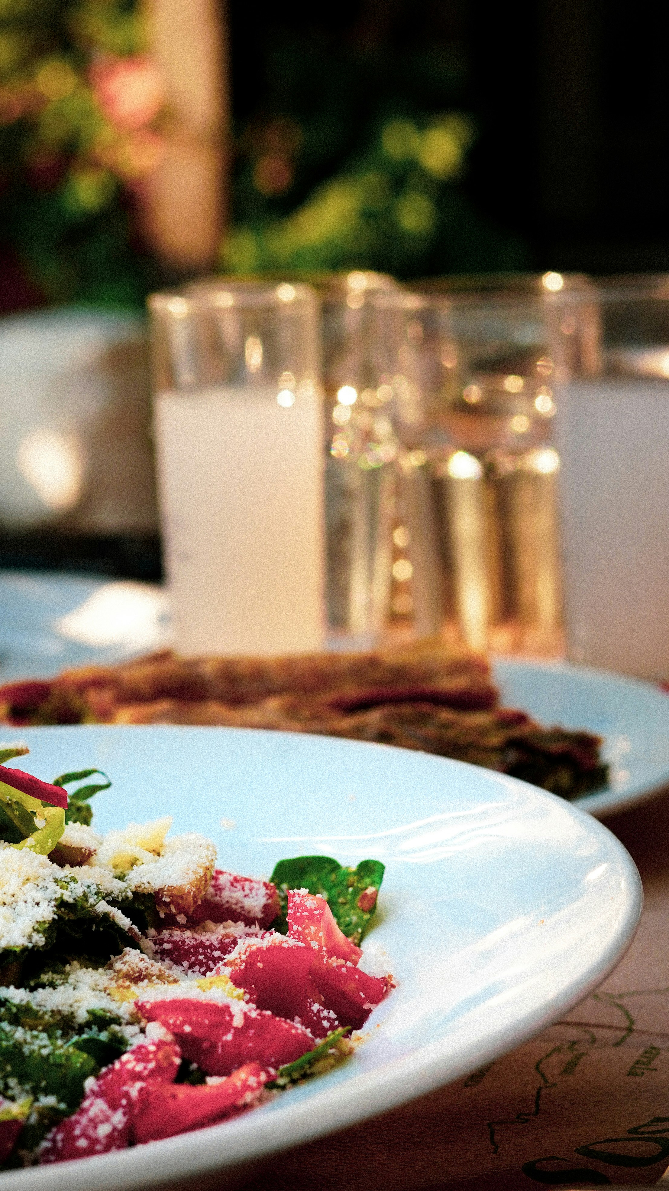 Une assiette de mezze méditerranéen et des verres de rakı laiteux posés sur une table de taverne, en soirée.