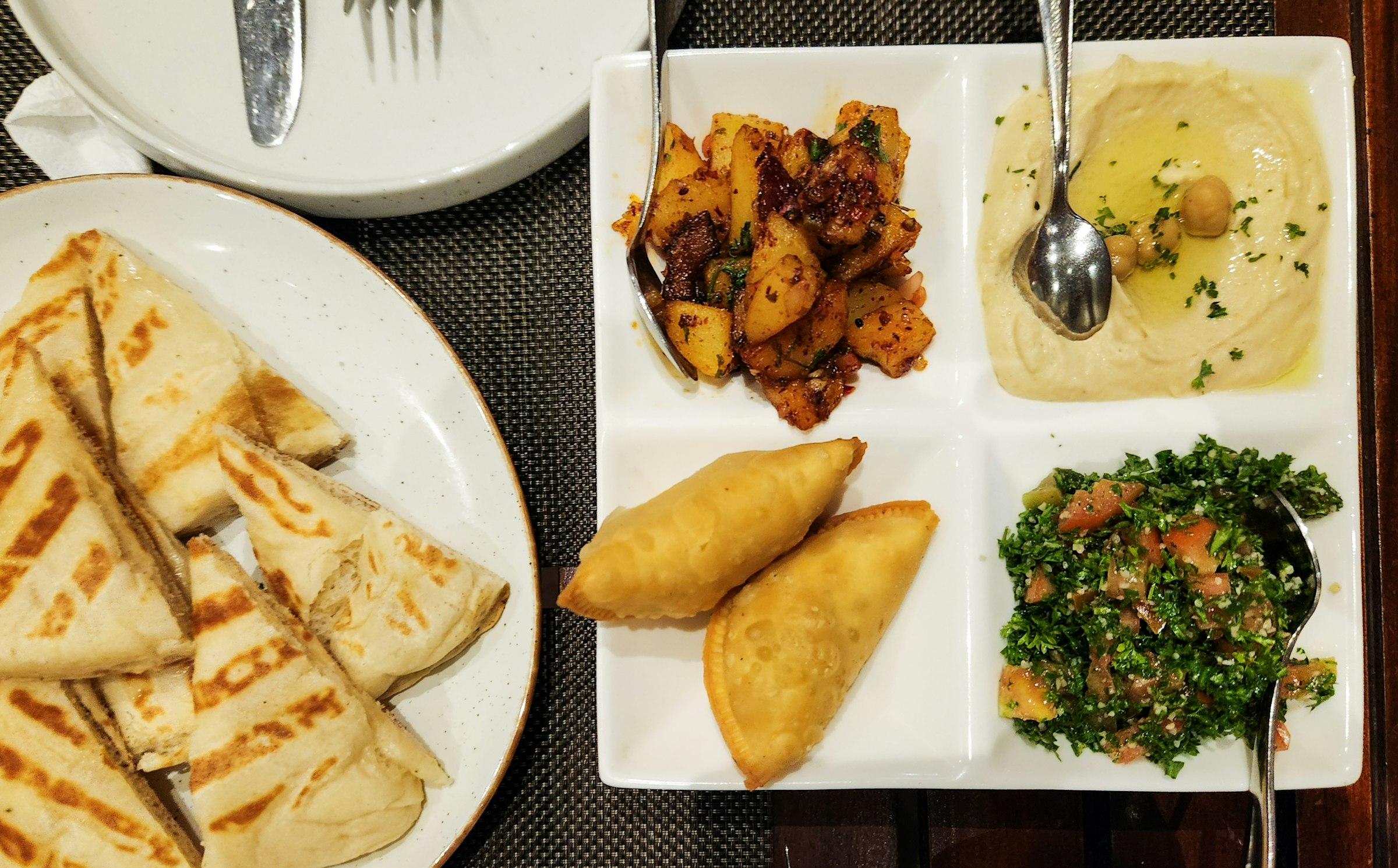 Un plateau de mezze — houmous, taboulé, pommes de terre épicées, petits chaussons frits et pointes de pita grillée.
