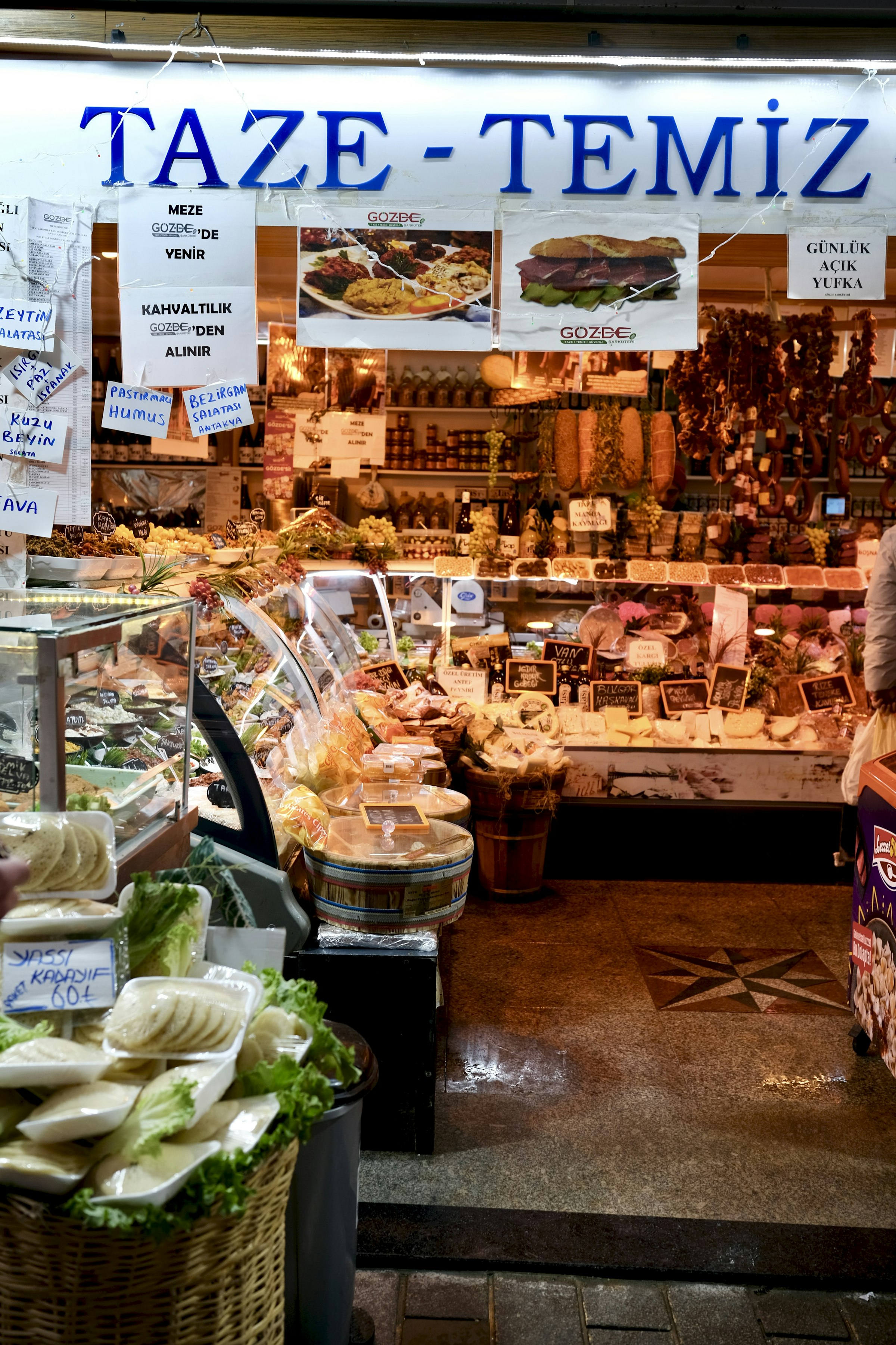 Un étal turc de produits frais — fromages, olives, mezze — sous une enseigne « TAZE-TEMİZ », denrées du matin alignées.