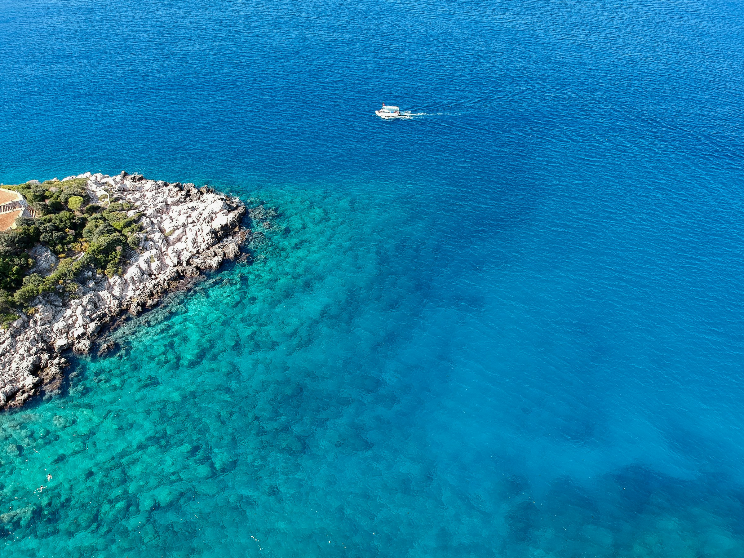 Vue aérienne d'une eau turquoise cristalline de la côte près de Kaş, une pointe rocheuse couverte de pins, un petit bateau.