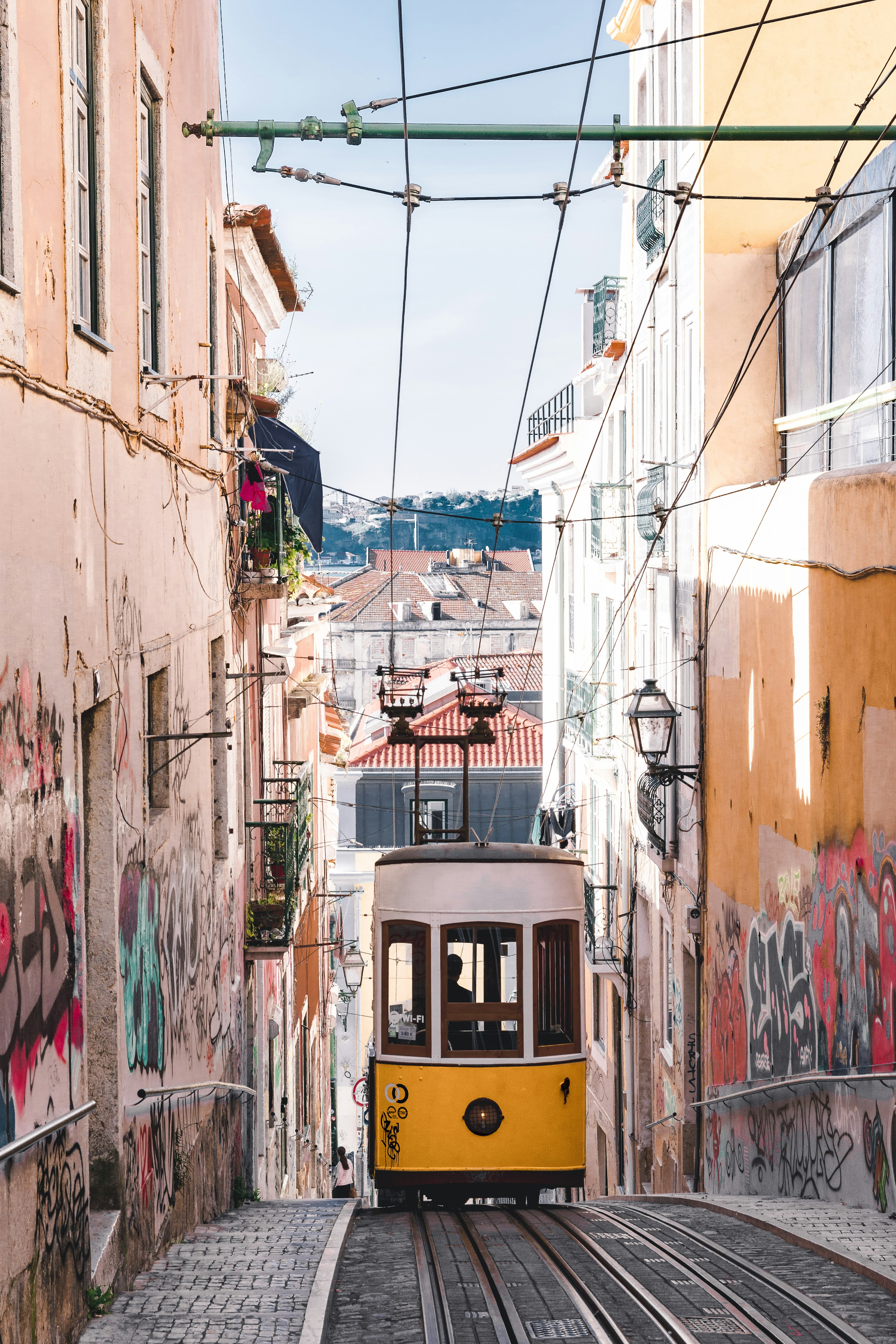 Tramway jaune et blanc de Lisbonne navigant dans une ruelle étroite bordée de vieux bâtiments — le tram iconique de Lisbonne dans le quartier historique de la ville.