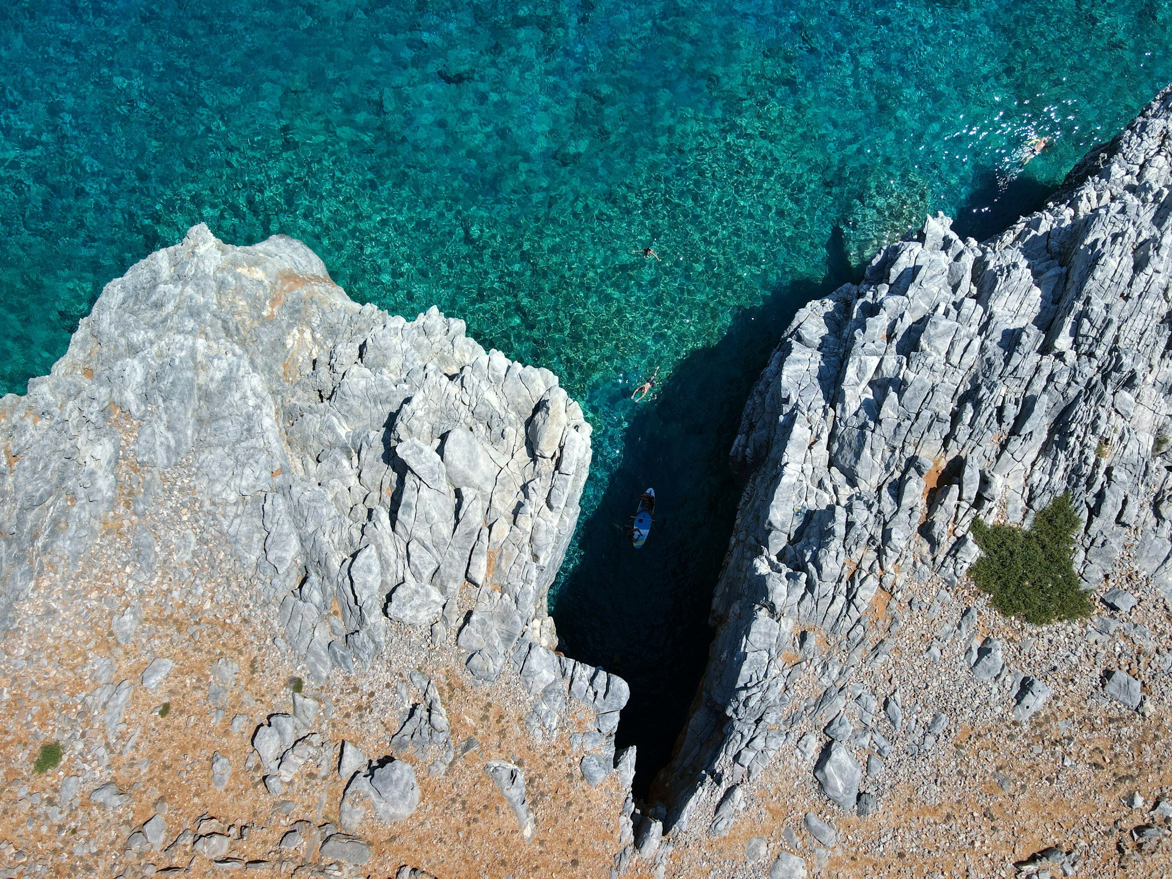 Vue aérienne d'une crique d'eau turquoise et translucide entre des rochers pâles, une petite plage de galets et un petit bateau — Marmara, près de Loutro.