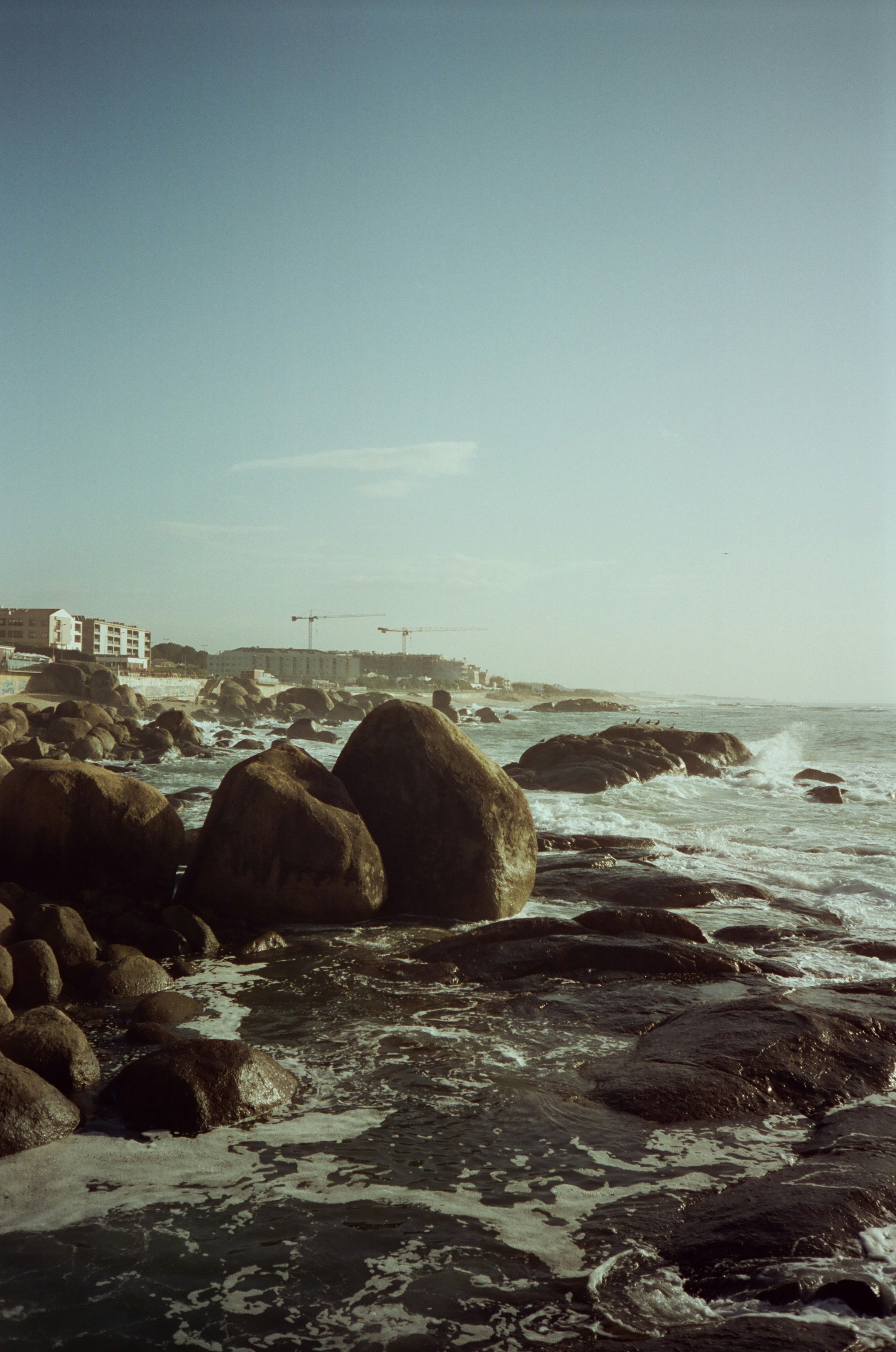 Des vagues de l'Atlantique s'écrasent sur une côte rocheuse de granite à Porto, des bâtiments au loin.