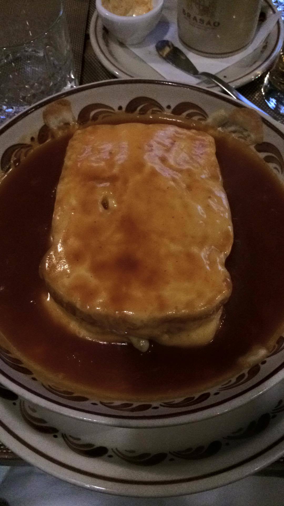 Une francesinha de Porto : sandwich recouvert de fromage fondu et nappé d'une sauce orangée épaisse, dans une assiette.