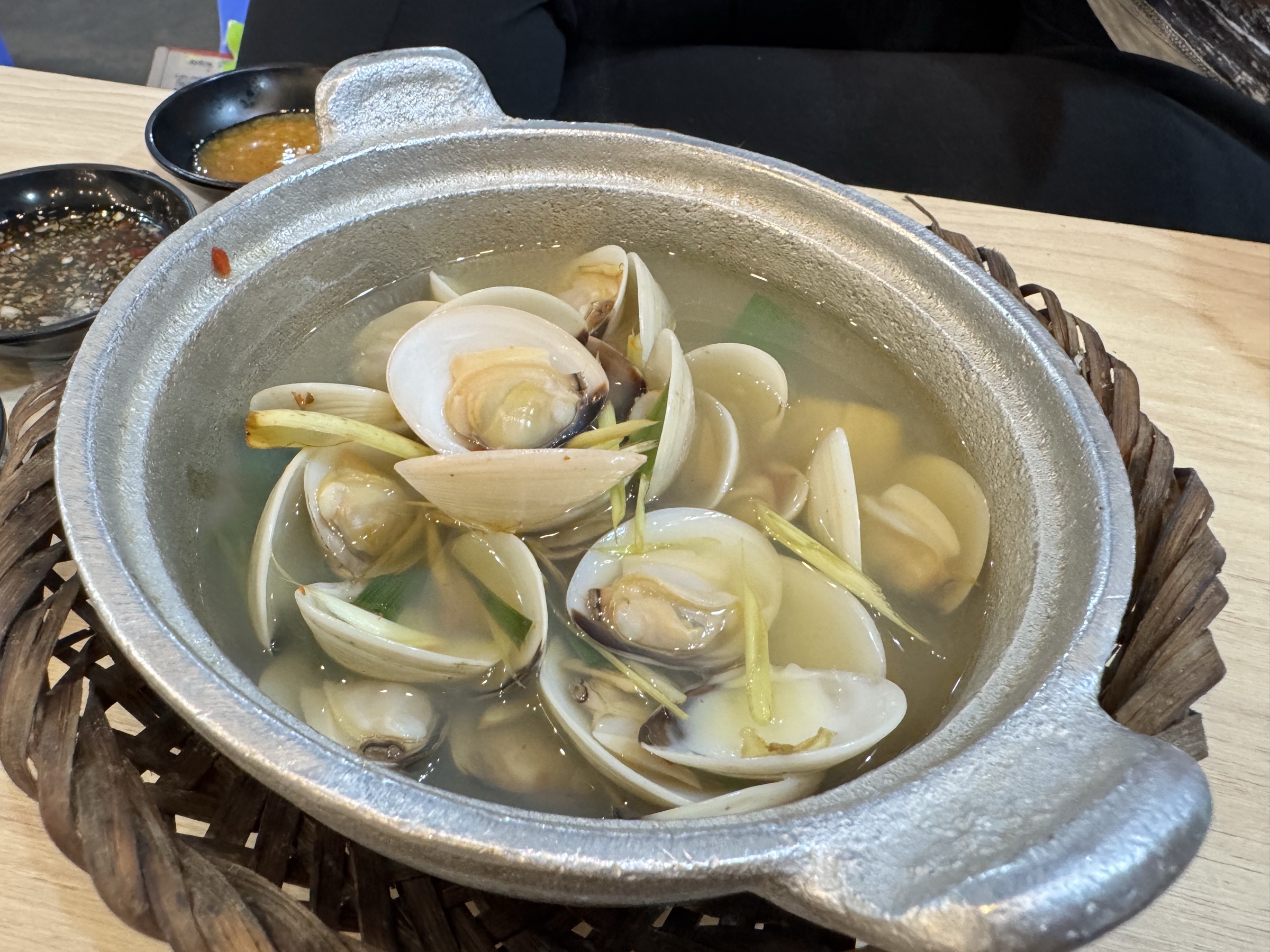 Cocotte de palourdes ouvertes (nghêu hấp) dans un bouillon clair au gingembre et ciboule, servie sur panier tressé avec deux sauces d'accompagnement, fruits de mer locaux de Quy Nhơn