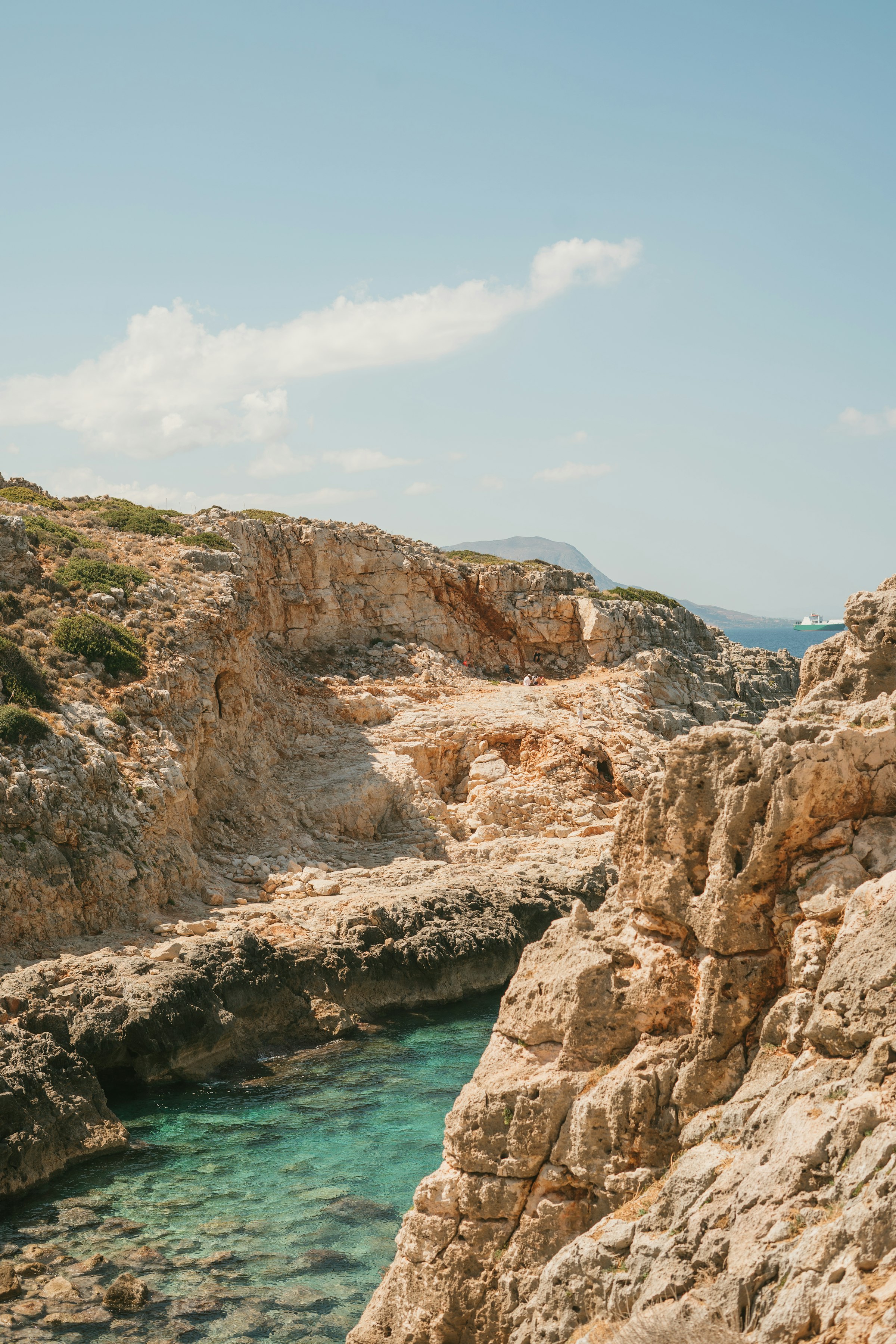 Une crique rocheuse isolée de la Crète : une eau turquoise cristalline entre des falaises dorées et arides, sans plage de sable, presque personne.