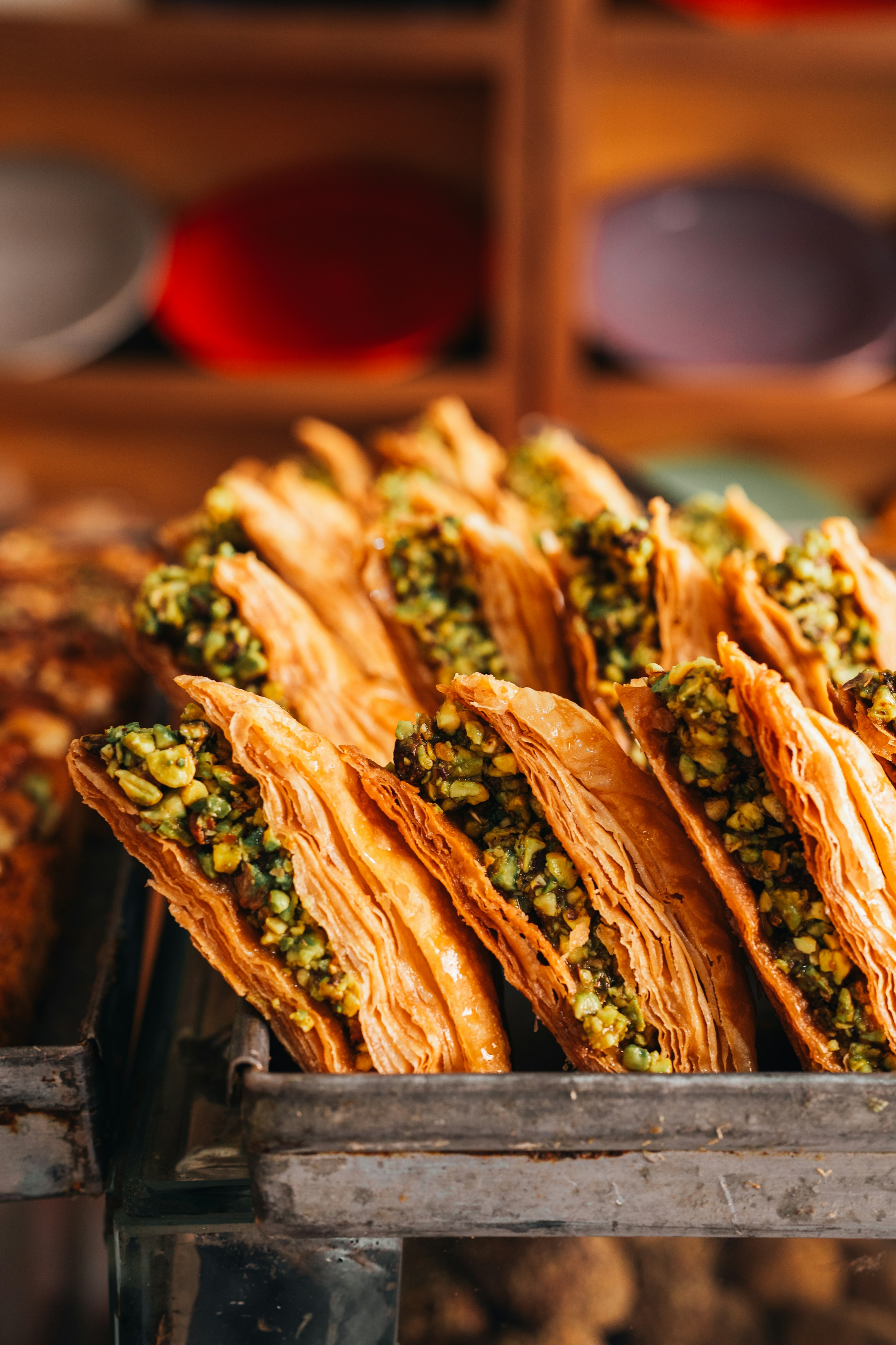 Des feuilletés de pâte phyllo dorée et croustillante, fourrés de pistaches hachées, serrés dans un plateau métallique — pâtisserie au miel, gros plan appétissant.