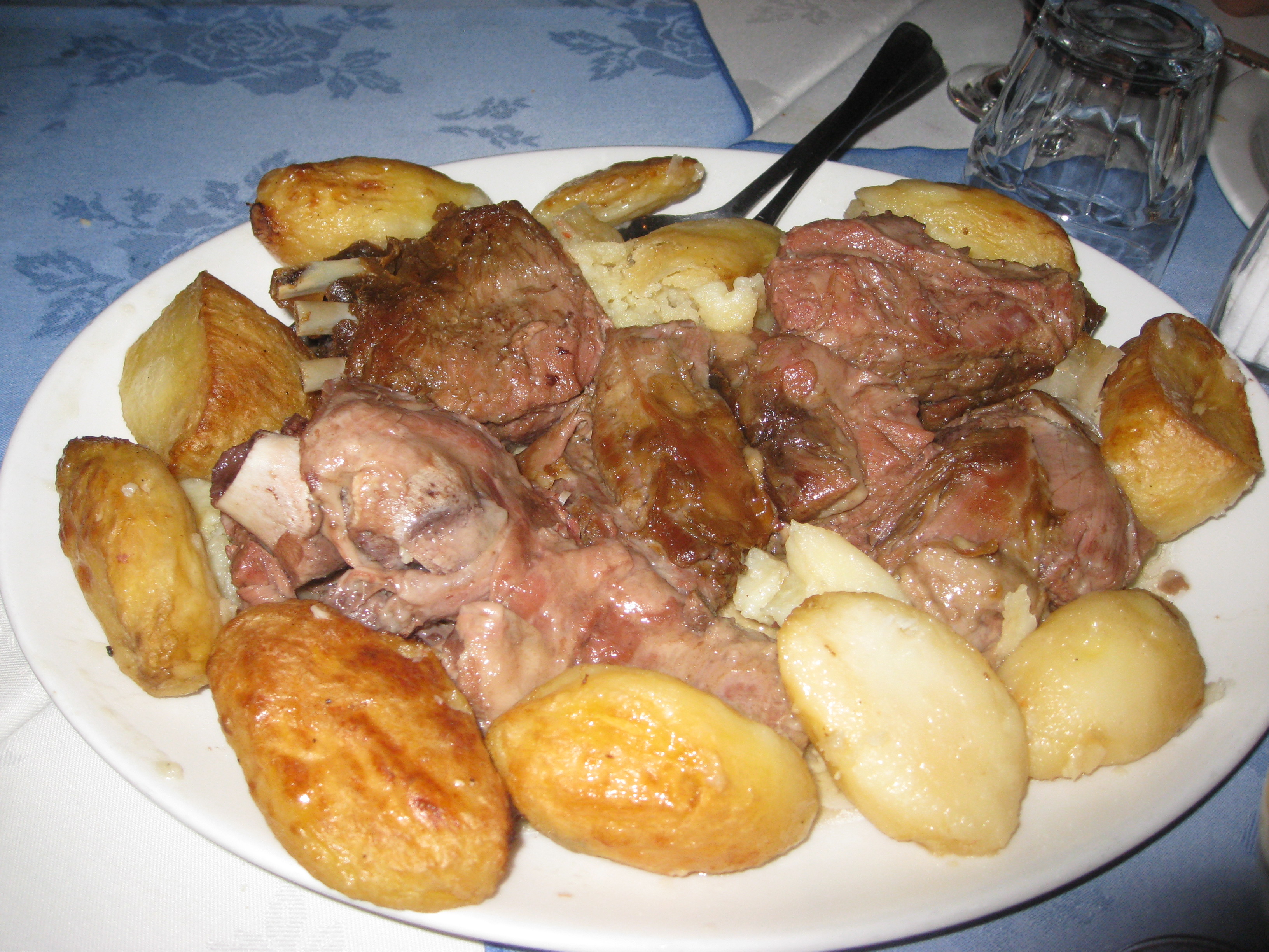 Un plat d'agneau cuit longuement, tendre et fondant, entouré de pommes de terre rôties dorées, sur une assiette blanche