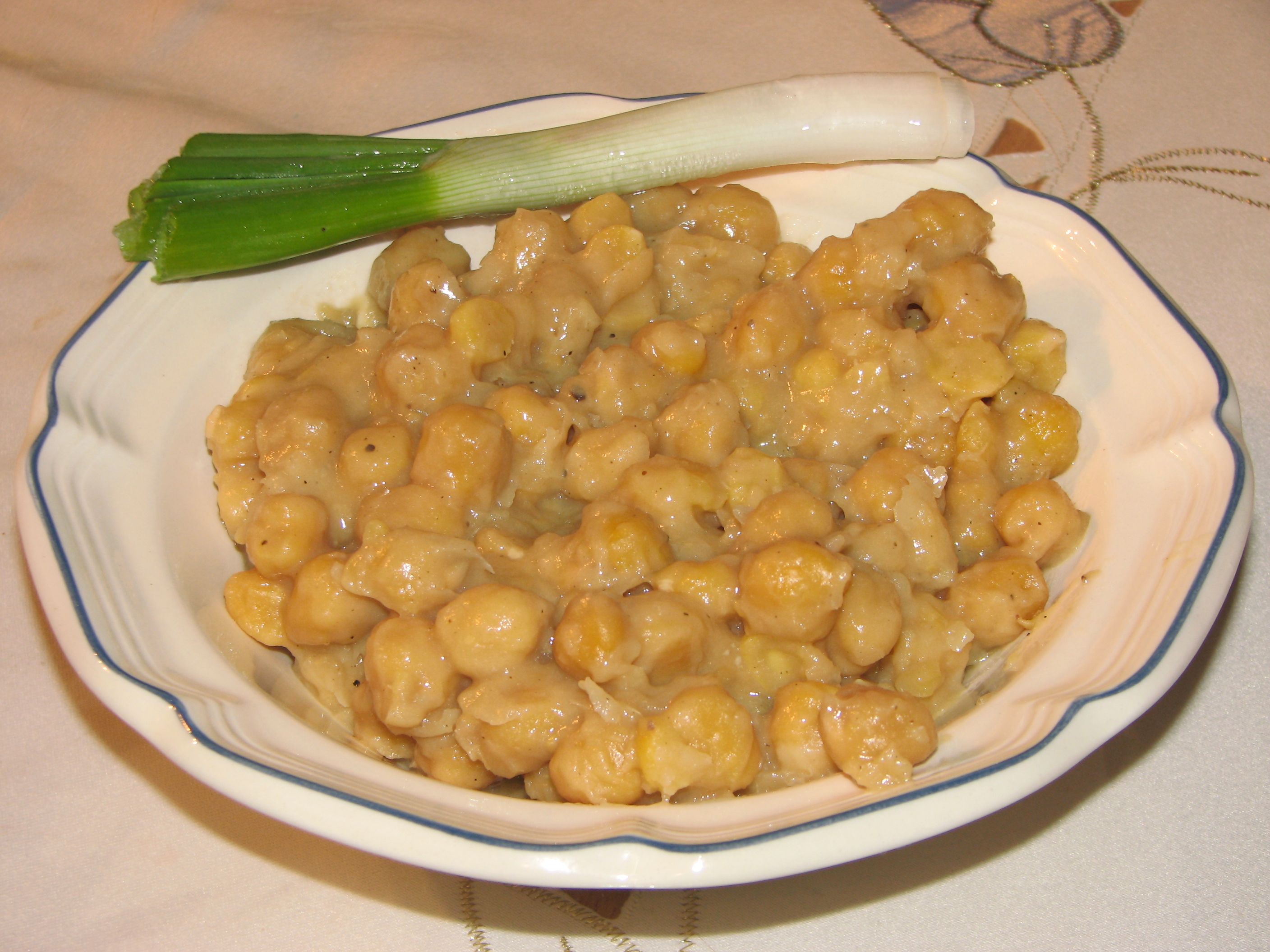 Un plat creux de pois chiches mijotés (revithada), crémeux et dorés, avec une tige d'oignon vert posée sur le bord